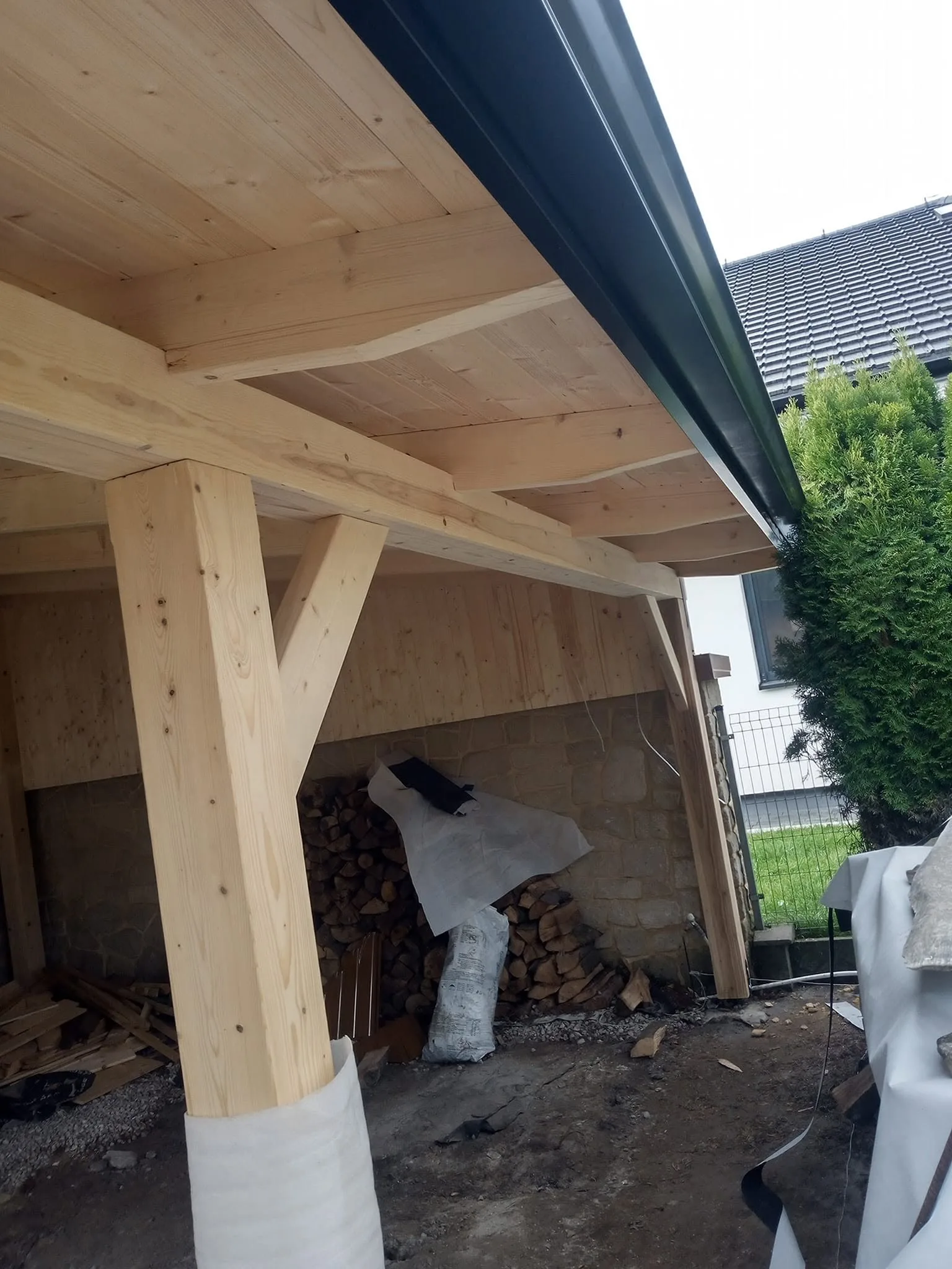 Konstrukcja drewnianej wiaty, w tle dach kryty blachodachówką