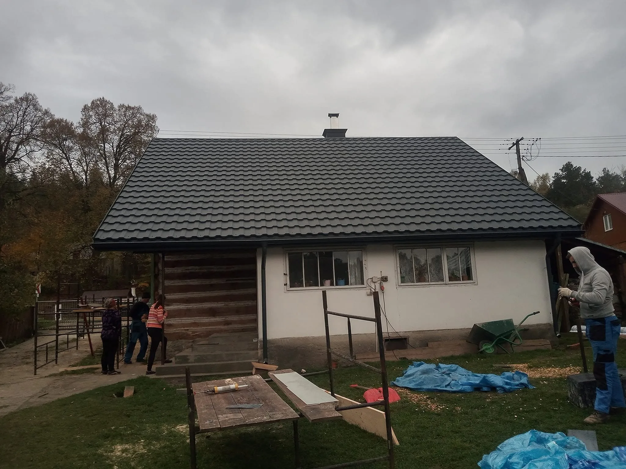 Dach kryty dachówką w kolorze grafitowym, widoczny komin i ekipa przy pracy